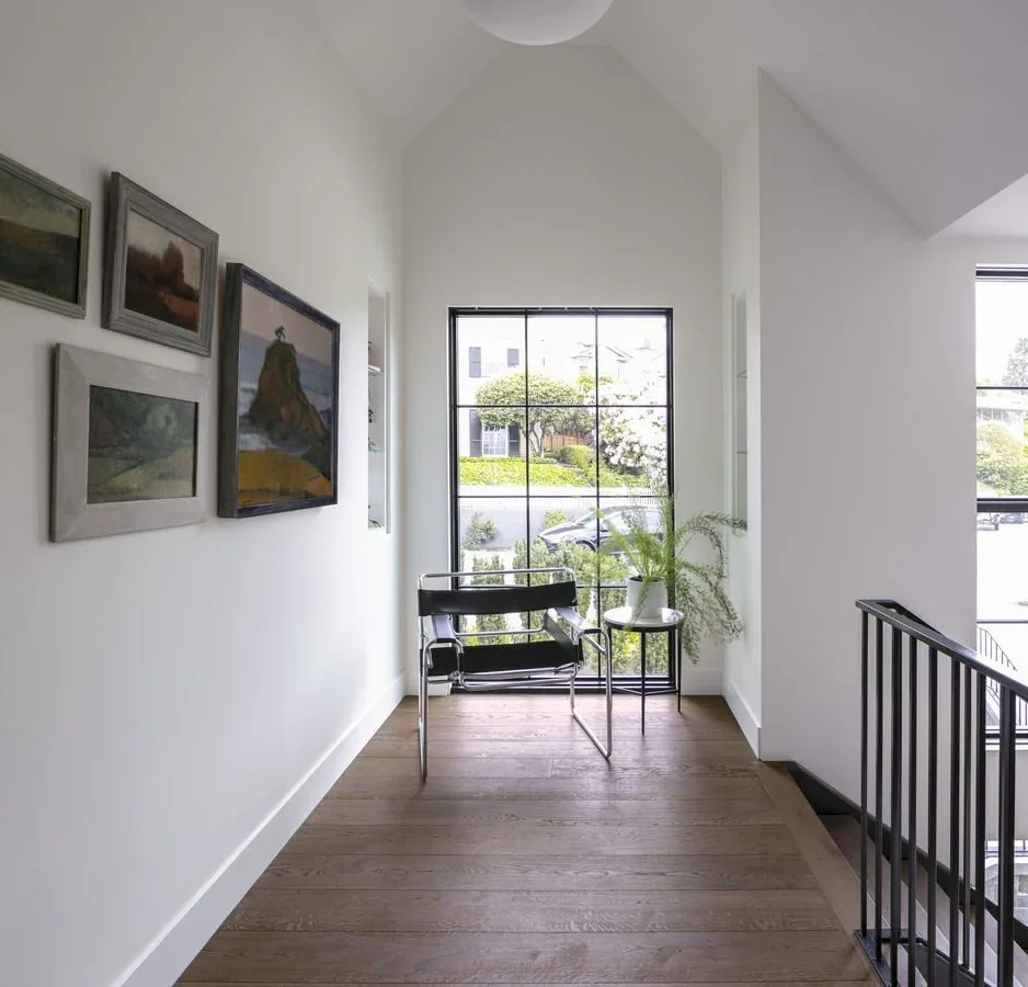 Upstairs hallway features vaulted ceiling, dark wood flooring, and large black-framed window with a view.