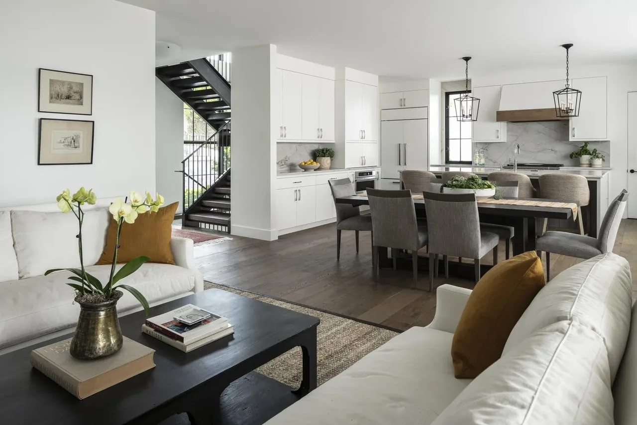 Open living, dining, and kitchen area with white cabinetry, dark hardwood floors, and gray fabric dining chairs.