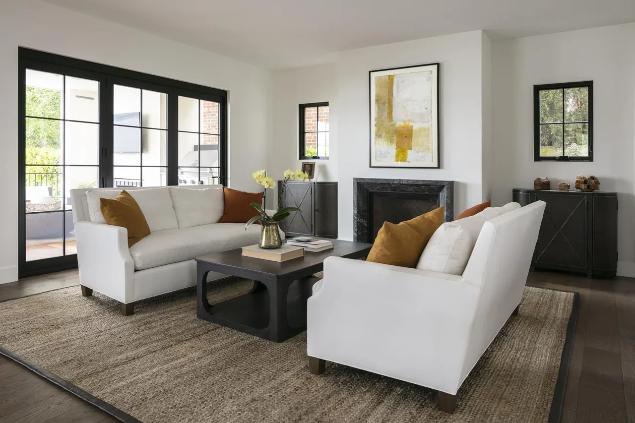 Living room features white sofas, a black fireplace, and black-framed sliding glass doors to an outdoor area.