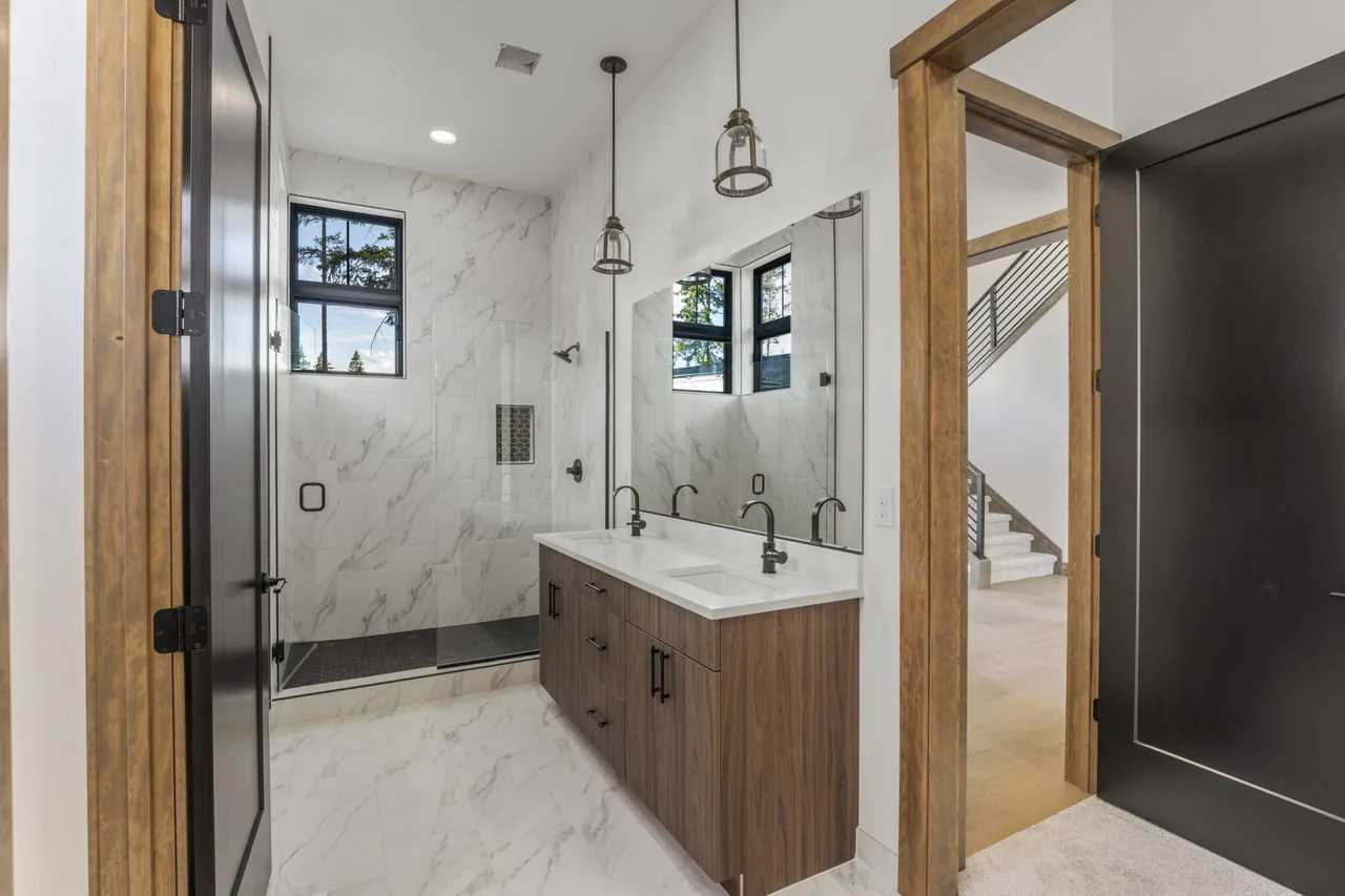 Bathroom features marble tile, double vanity with wood cabinetry, pendant lights, and glass shower enclosure.