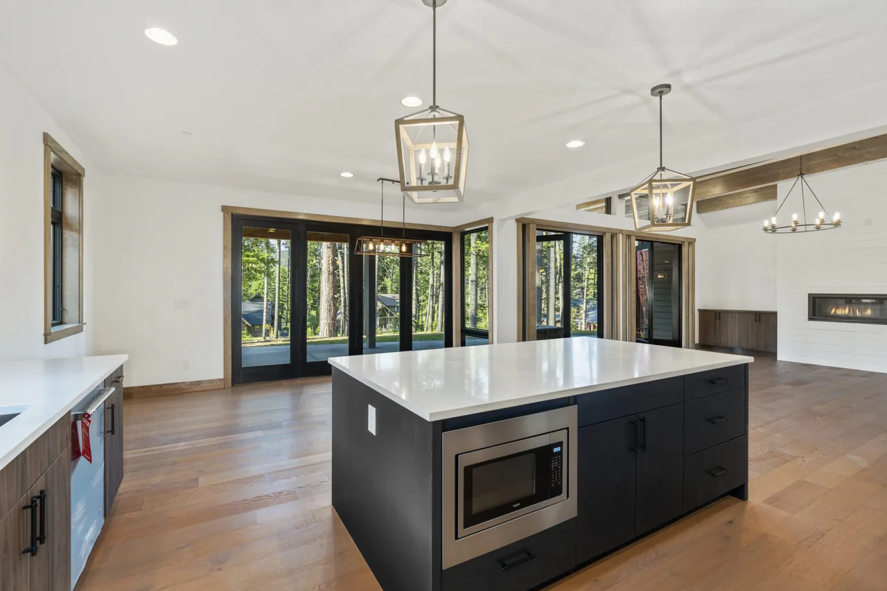 Kitchen with large island, black cabinetry, wood floors, and adjacent living area with fireplace and exposed beams.