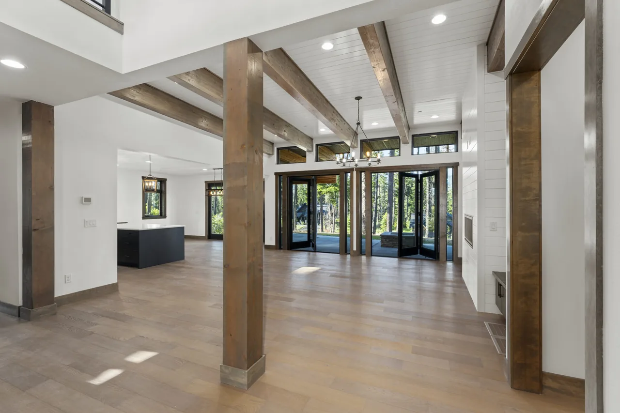 Open floor plan living room featuring exposed wood beams and large pivot glass doors leading outdoors.