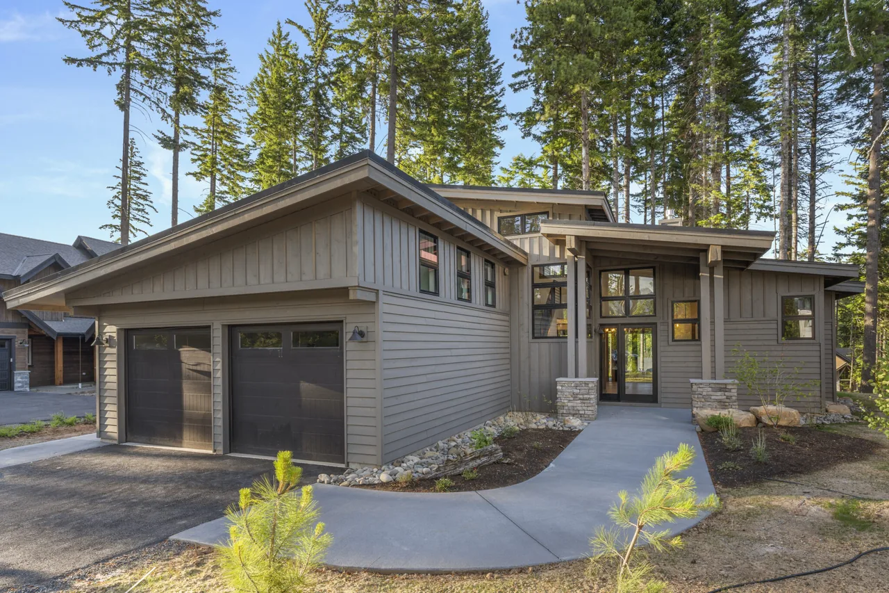 Modern one-story house with board and batten siding, double garage, and a covered entry with stone pillars.