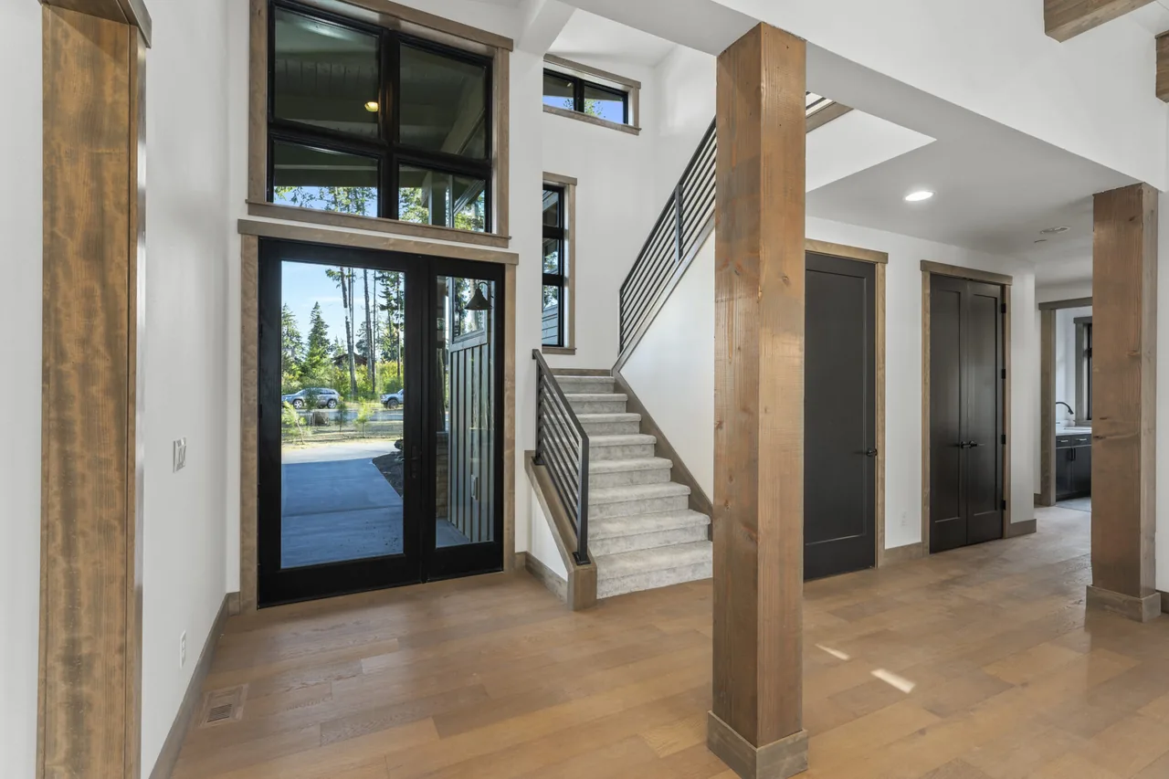 Entry area featuring black-framed glass doors, a staircase with metal railing, and wooden columns and flooring.