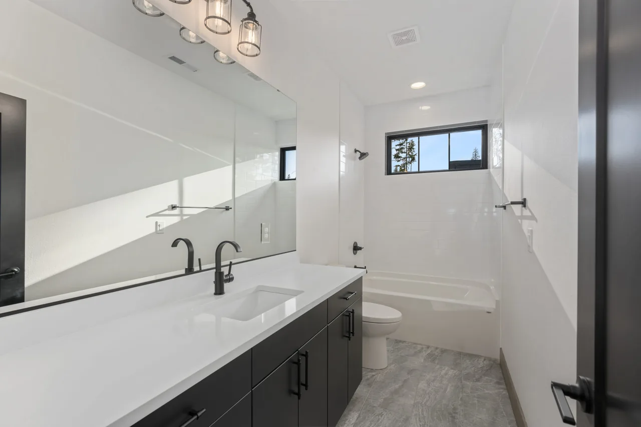 Bathroom features a long countertop vanity with black fixtures and cabinetry, with a small window over the bathtub area.