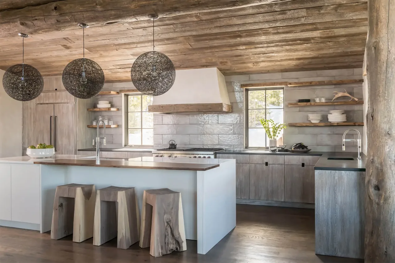 The kitchen features natural wood finishes, a white island with wood countertop, and three sculptural wooden stools under woven pendant lights.