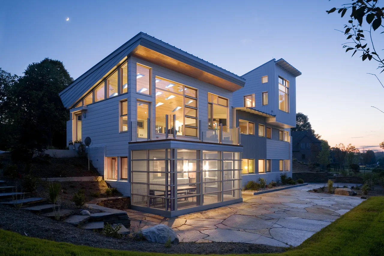 Copy of Crotty Hall by Sigrid Miller Pollin features a modern sloped roofline with extensive illuminated windows and stone patio.
