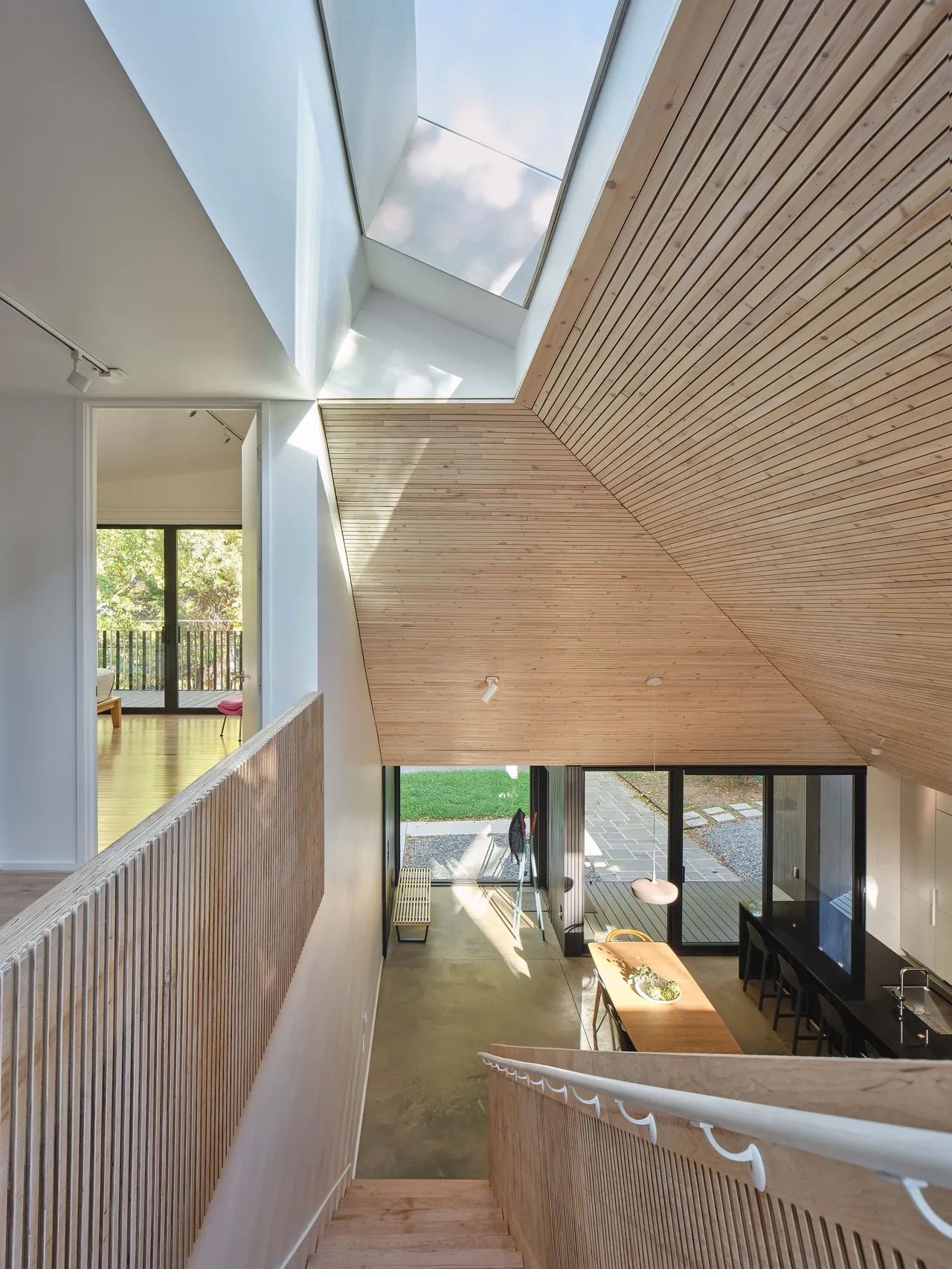 Modern interior with a wood-paneled vaulted ceiling, large skylight, and floor-to-ceiling glass doors opening to an outdoor patio.