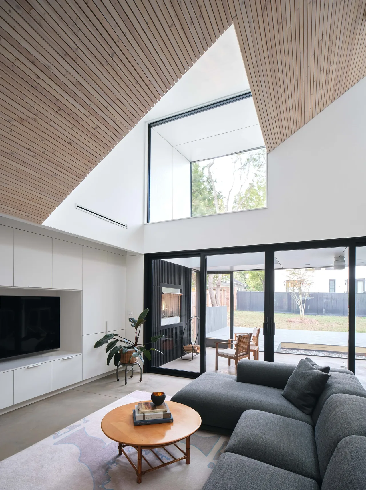 Living room features a vaulted ceiling with wood paneling, large corner window, and black-framed sliding glass doors to a patio with fireplace.
