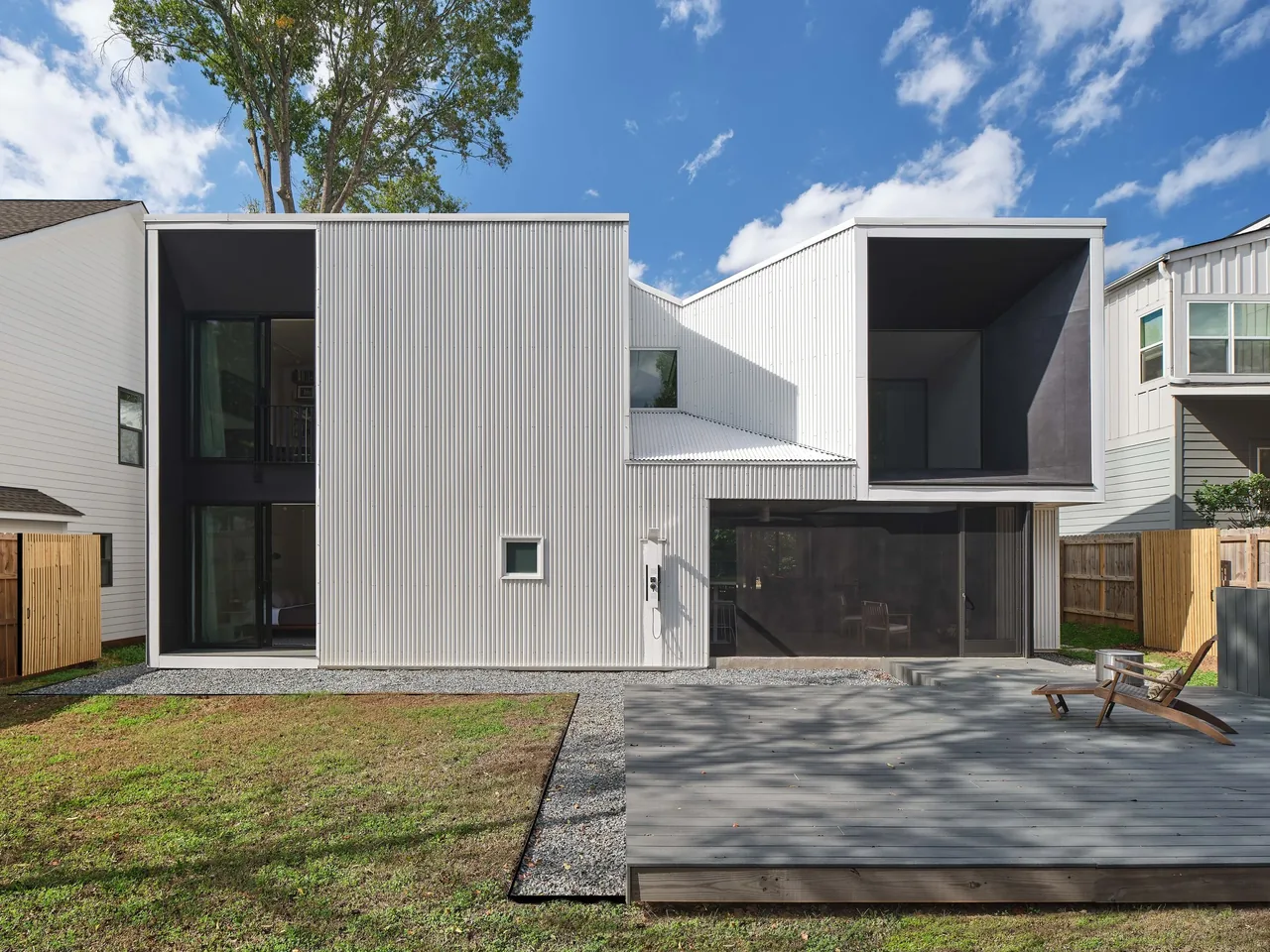 The rear of the Steel Louise project features corrugated siding, large windows, and a recessed balcony under a flat roof.