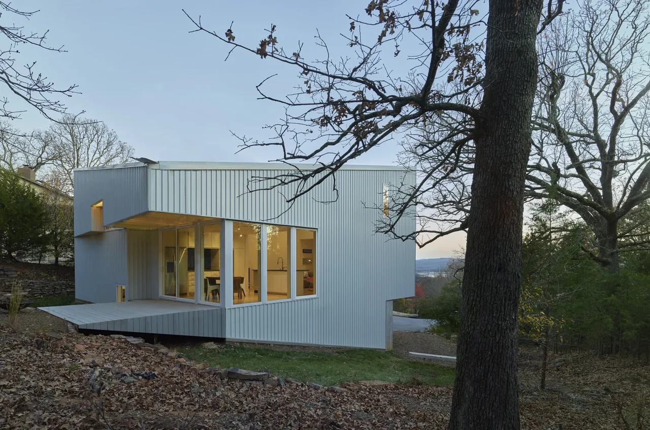 Hillside Rock features vertical metal siding and large windows that open to natural woodland surroundings.