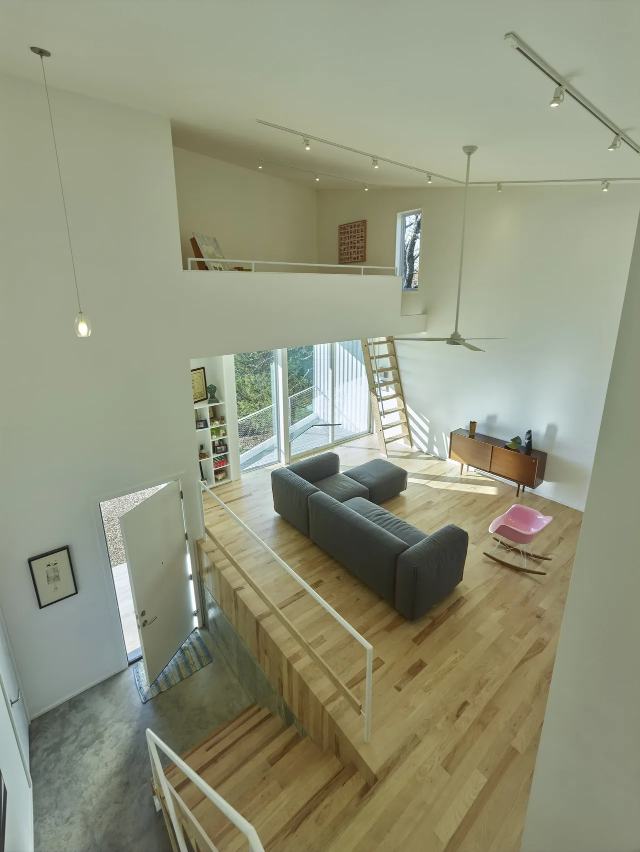 Living room area with a gray sectional sofa, pink rocking chair, and large windows opening to a balcony.