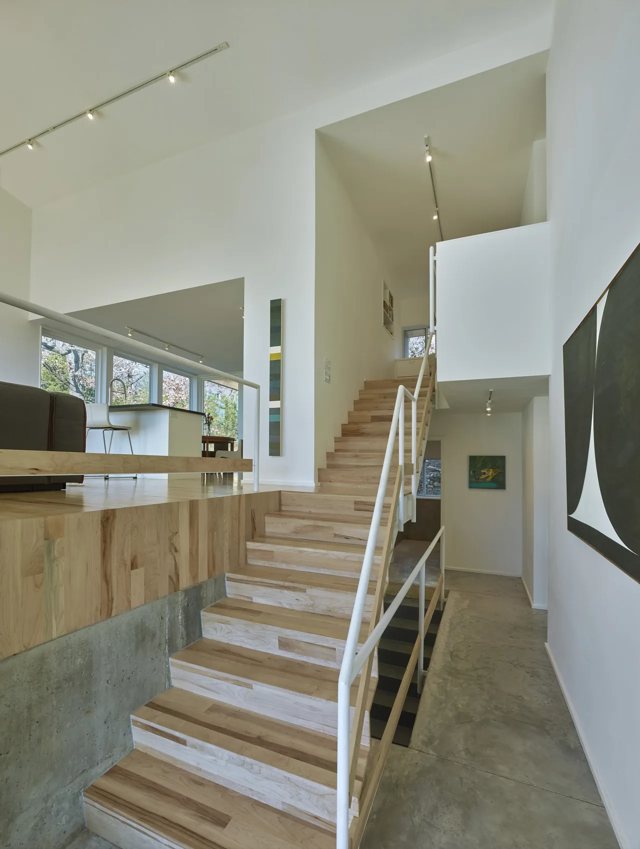 Modern interior stairs with light wood treads, white railing, and concrete flooring in Hillside Rock project by SILO.
