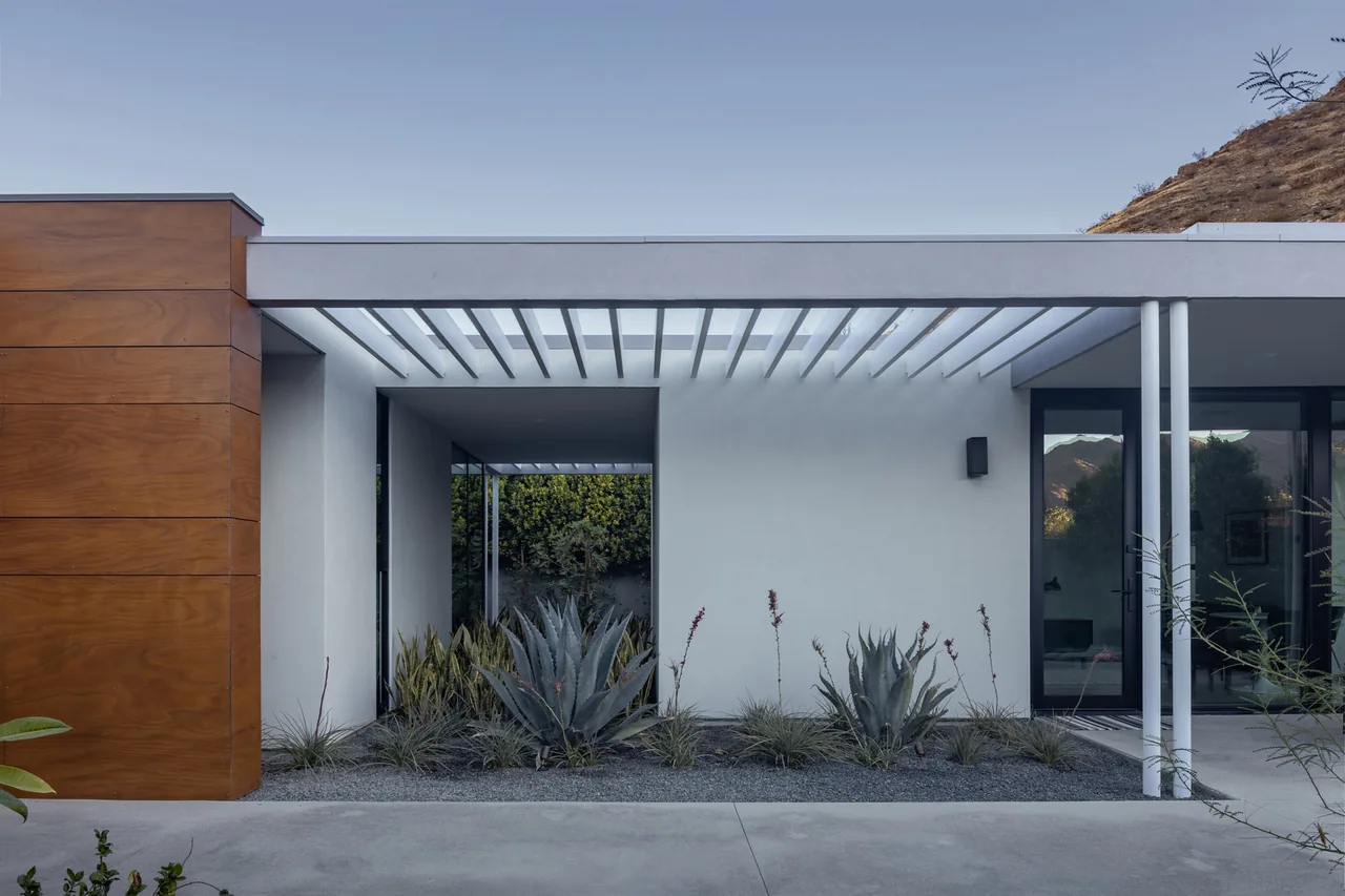 Modern home exterior featuring white stucco walls, wooden paneling, a pergola, and drought-tolerant landscaping.