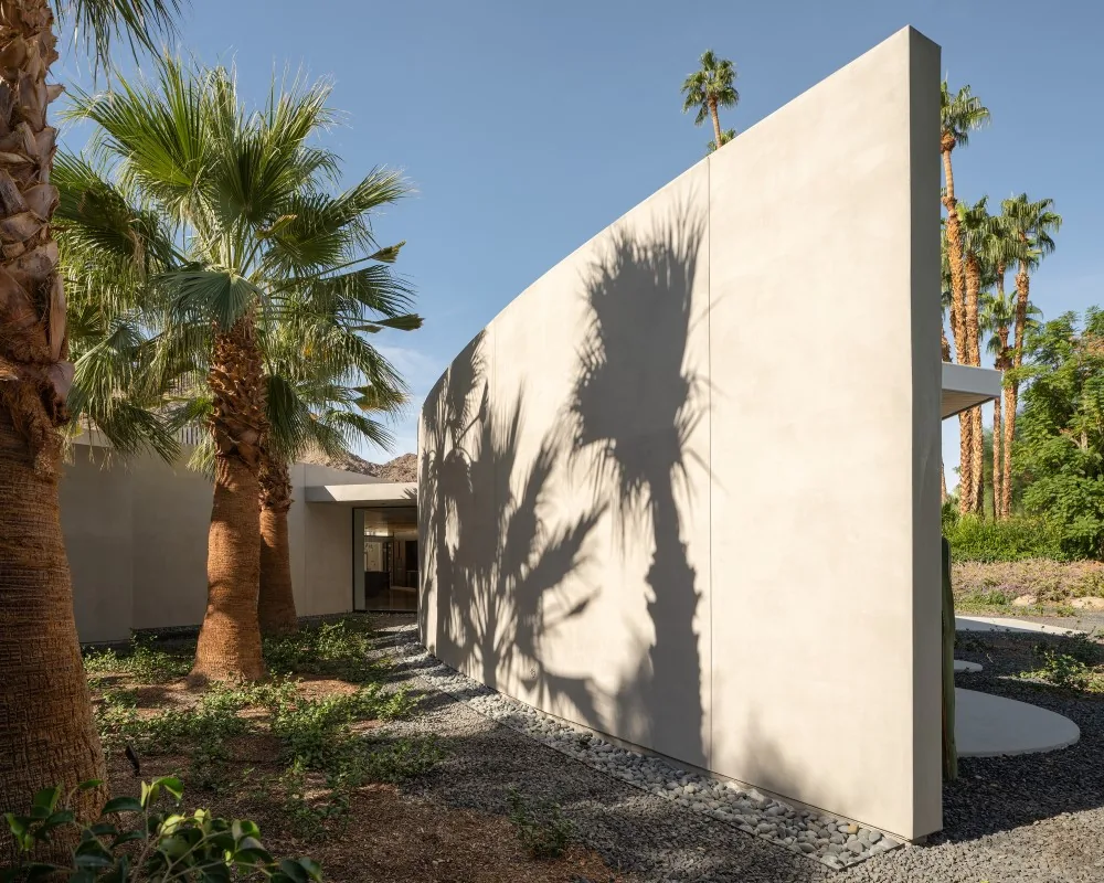 Curved light-colored plaster exterior wall with palm trees casting shadows at Eldorado Tres project.