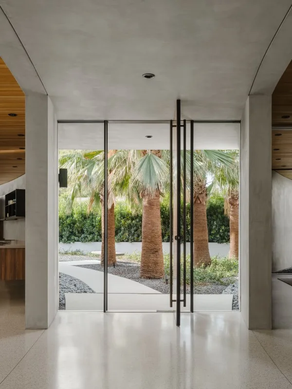 Glass entry doors open to a landscaped courtyard with palm trees and a curving path at Eldorado Tres.
