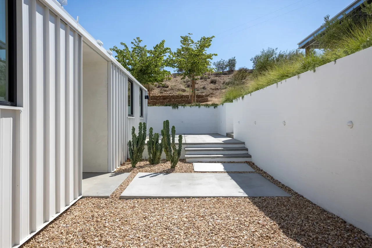 Outdoor patio area with white stucco retaining walls and steps, plus metal vertical siding on the adjacent building.
