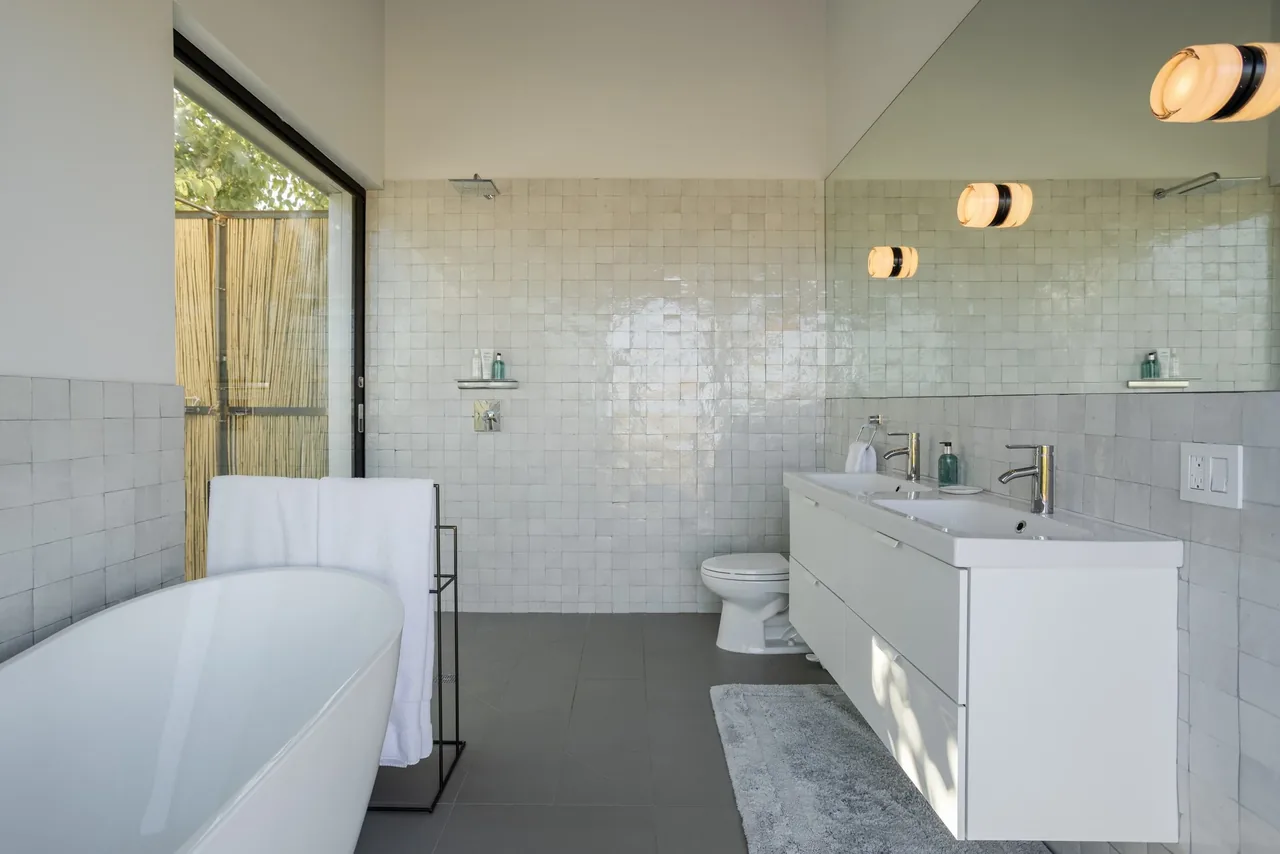 This bathroom features a freestanding tub, wall-mounted double vanity, and white tile walls with a large mirror.