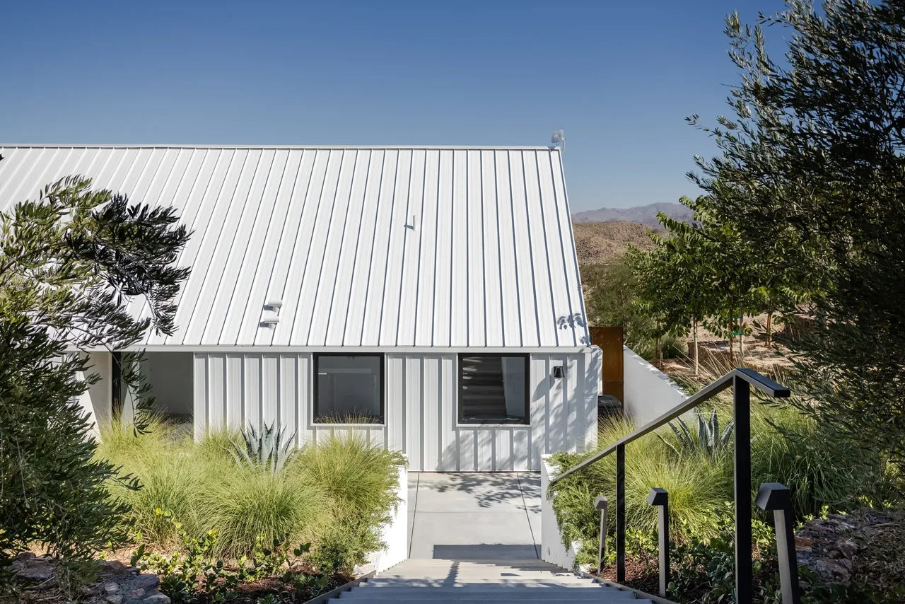 The Alta guesthouse features a white metal standing seam roof, vertical siding, and tiered concrete steps surrounded by desert landscaping.