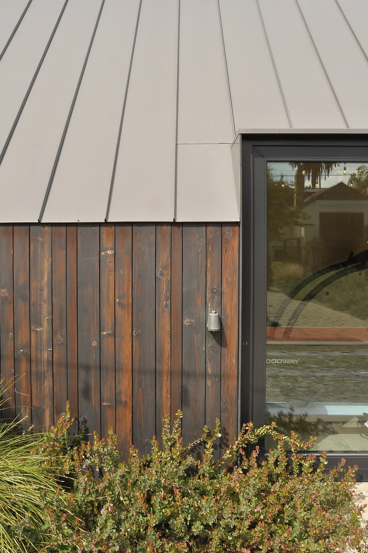 Exterior wall of Bellefontaine Studio showing charred wood siding, a standing seam metal roof, and a glass door with black frame.