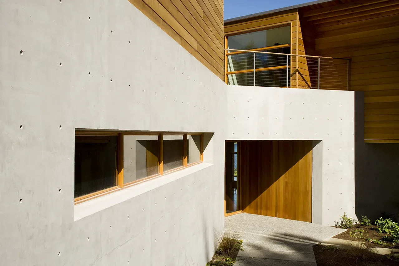 The Y House by Peter Cohan Architect shows modern design with concrete and wood materials and a balcony above the entry.