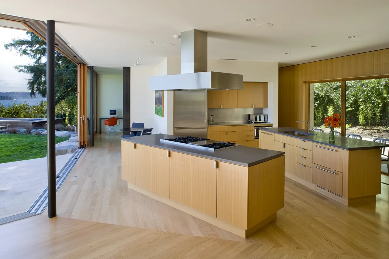Kitchen of Y House with wood cabinetry, two islands with cooktop and sink, and expansive folding glass doors opening to the outdoors.