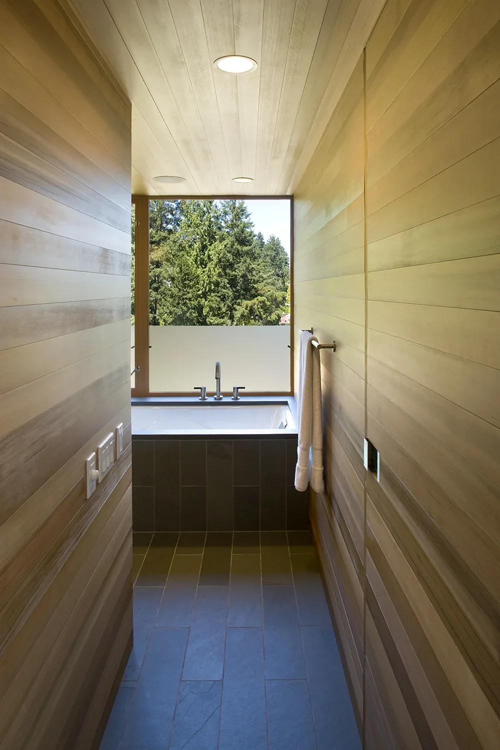 Bathroom in Y House by Peter Cohan Architect features horizontal wood-paneled walls and a large window with forest views.