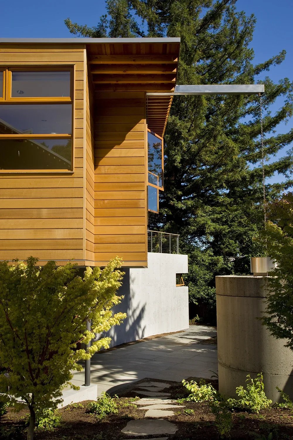 Y House features horizontal wood siding, a flat roof with exposed beams, and a concrete foundation nestled in greenery.