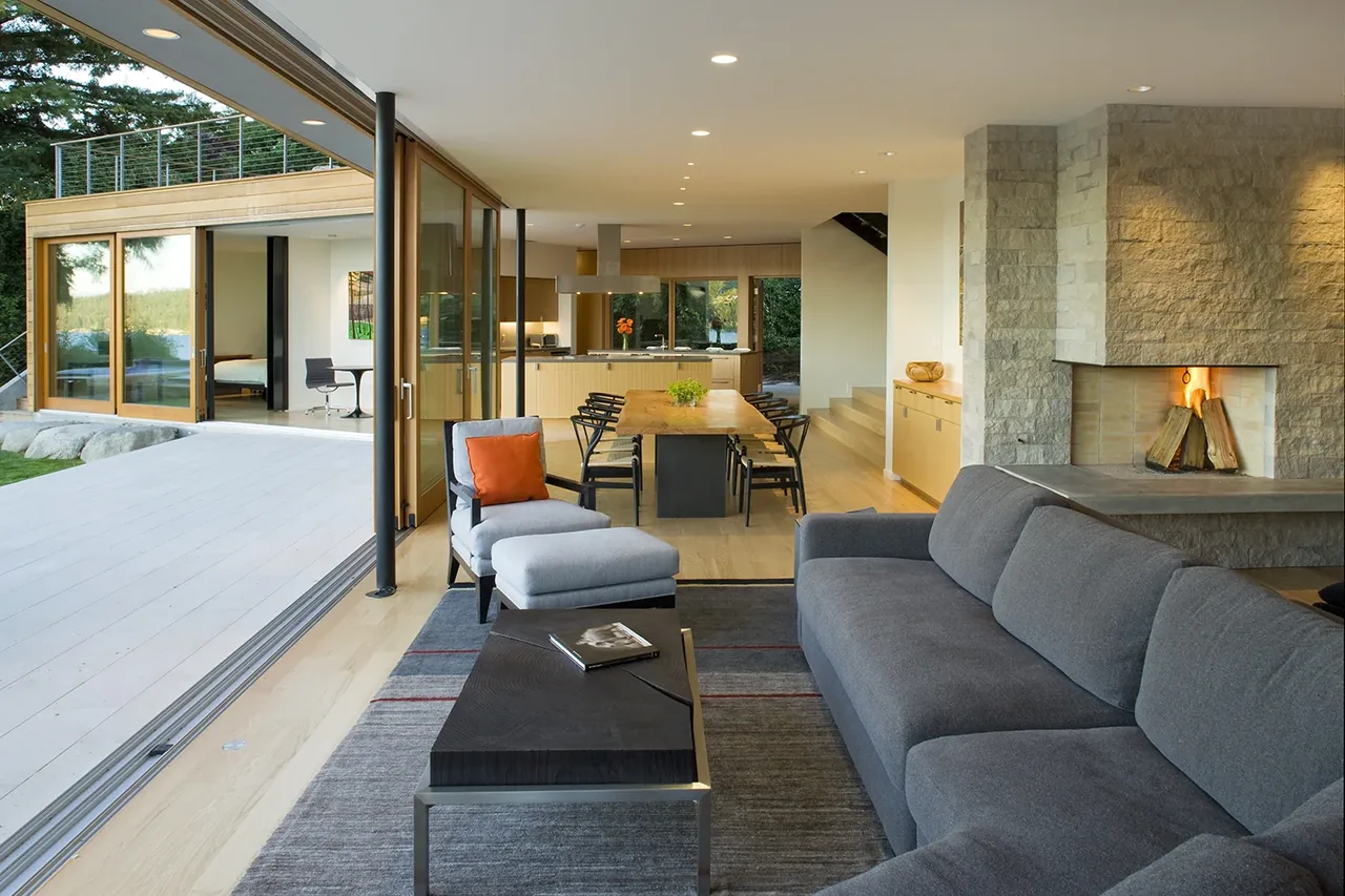 Open floor plan connecting living room with stone fireplace and dining area featuring a live edge wood table and folding glass doors to the outdoor patio.