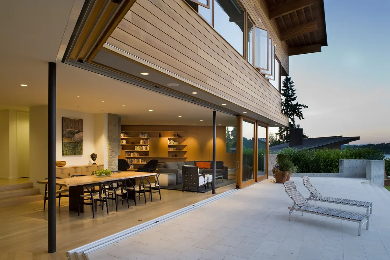 Y House by Peter Cohan Architect features folding glass doors that open an indoor living and dining space to the outdoor patio with lake views.