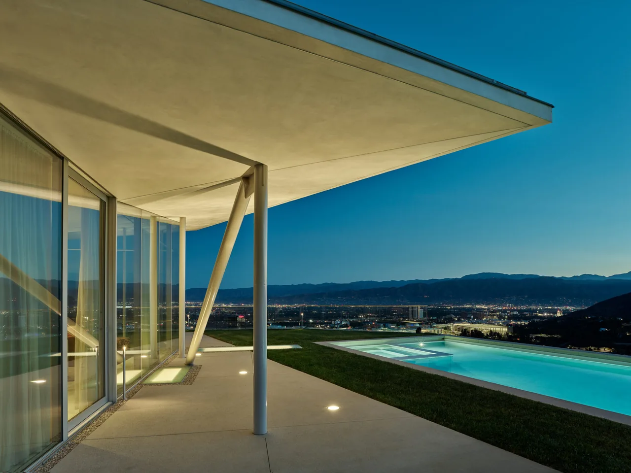 Modern California house exterior at night featuring large floor-to-ceiling windows and a pool with city views.