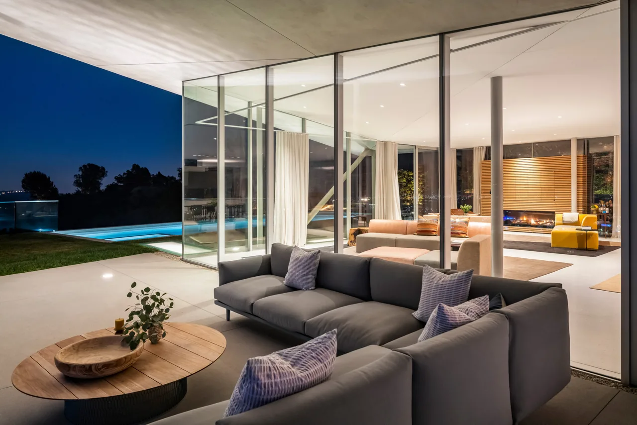 California House features floor-to-ceiling glass walls and an outdoor living area overlooking a pool at night.