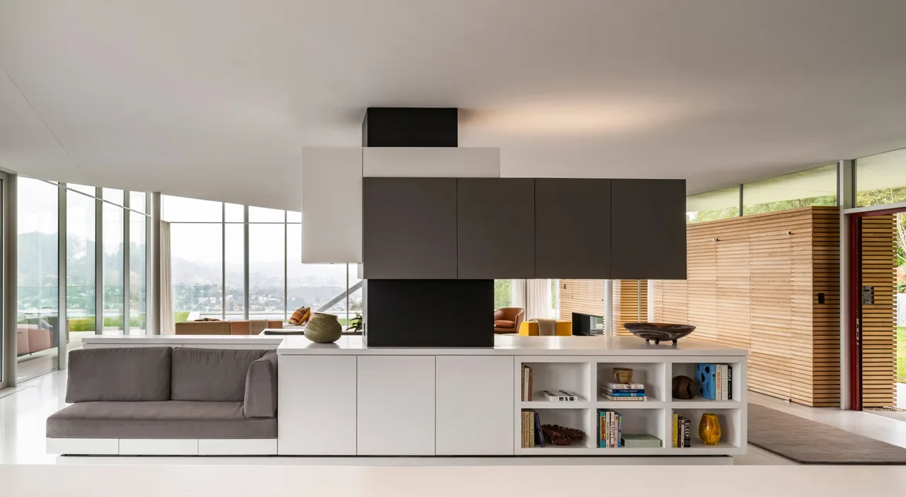 Built-in cabinetry with integrated sofa separates the living space with large windows and wooden panel walls.
