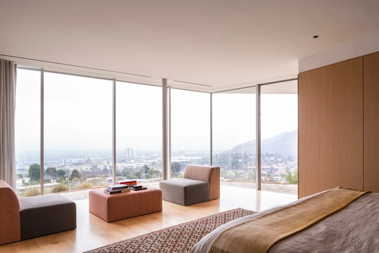 Bedroom with corner floor-to-ceiling glazing and cityscape with mountain views through glass walls.