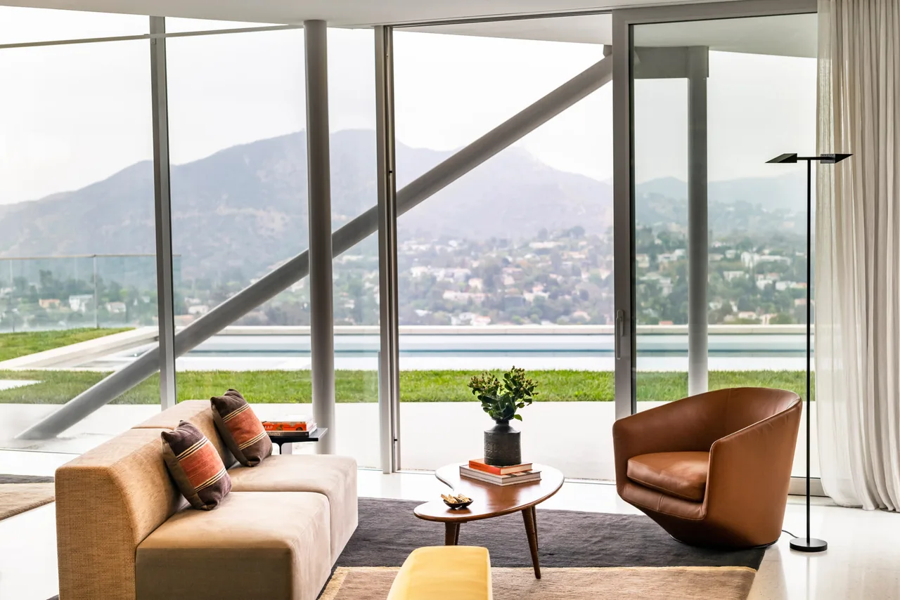 Mid-century style living area with floor-to-ceiling glazing and glass door opening to a pool and hillside view.