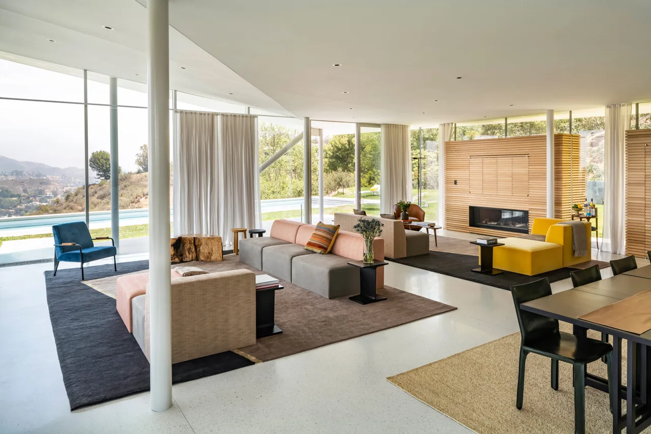 Open-plan living room with expansive glazing and a wood-paneled fireplace in California House by GLUCK+.