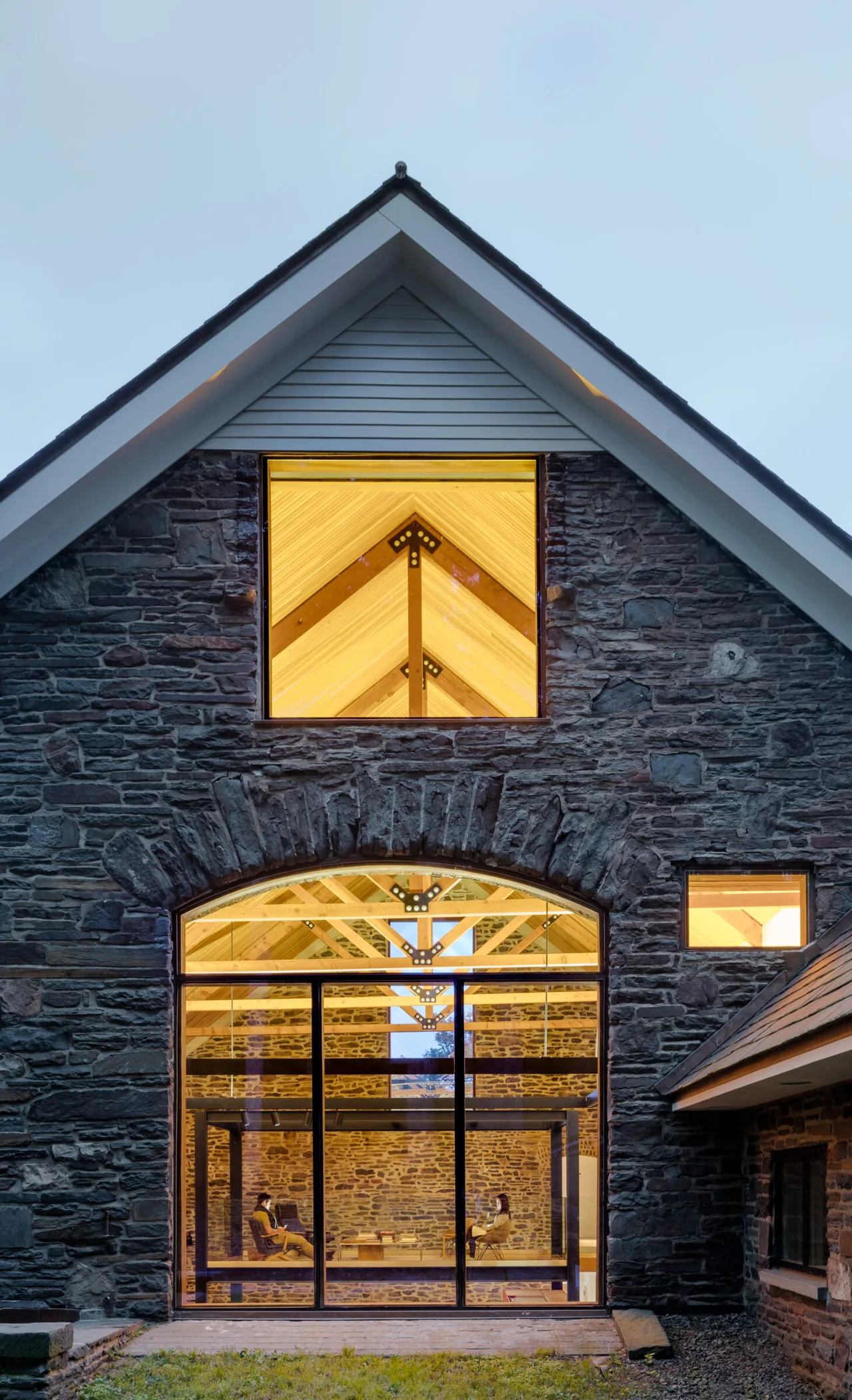 Renovated barn with exposed wooden beams and large black-framed glass windows showcasing interior seating.