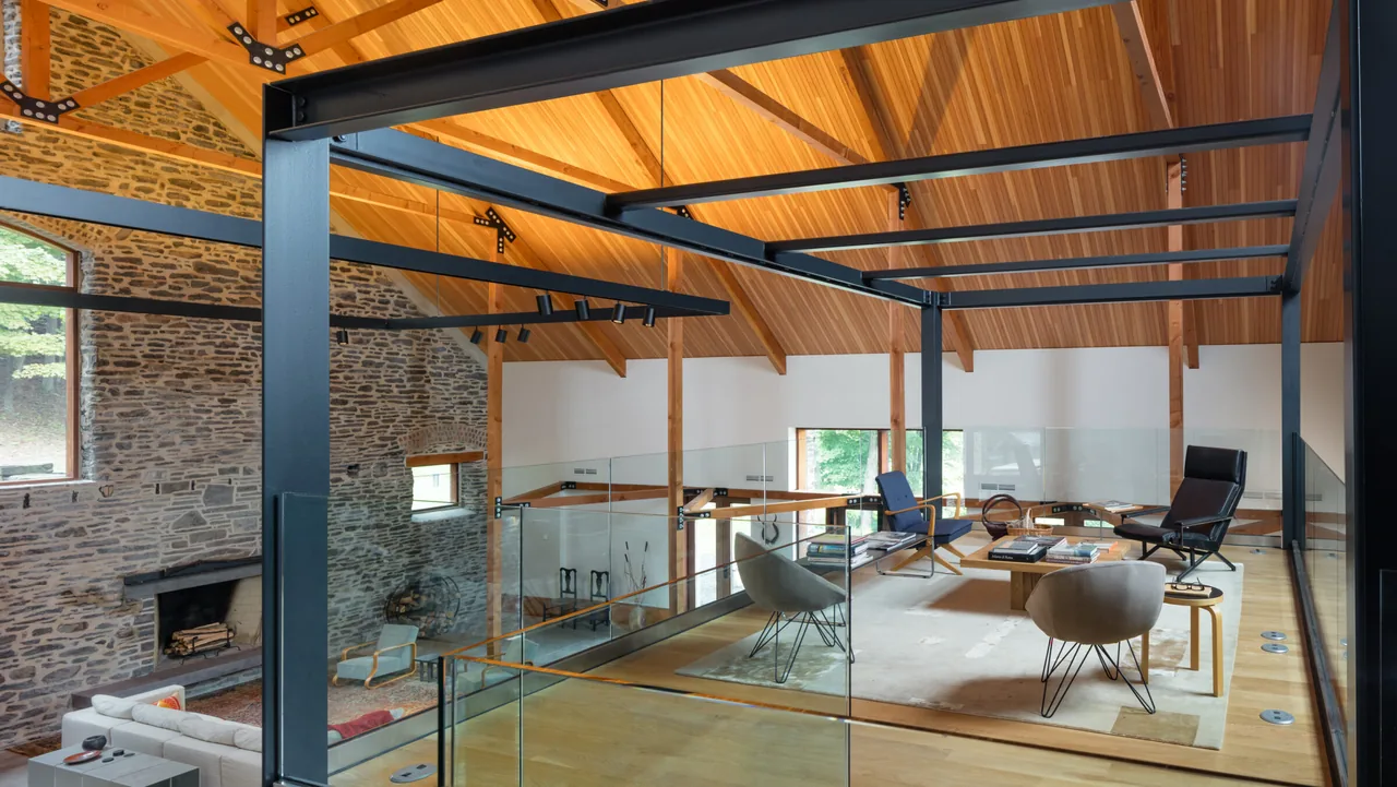 Barn-style living area with exposed wood ceiling, stone masonry wall, and steel structural beams around seating area.