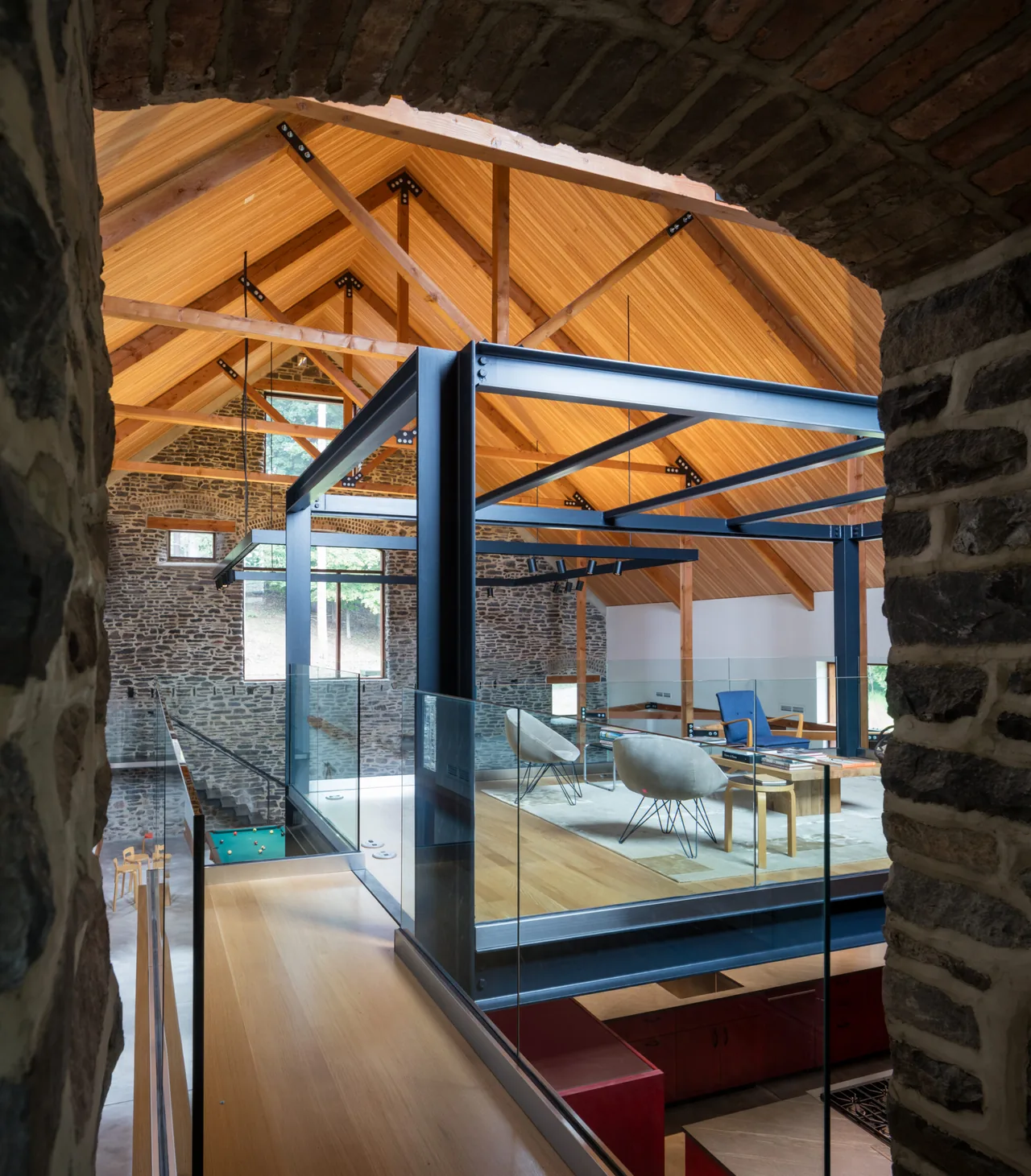 Living area features exposed wood trusses and stone masonry walls, combining rustic barn elements with modern steel framing.