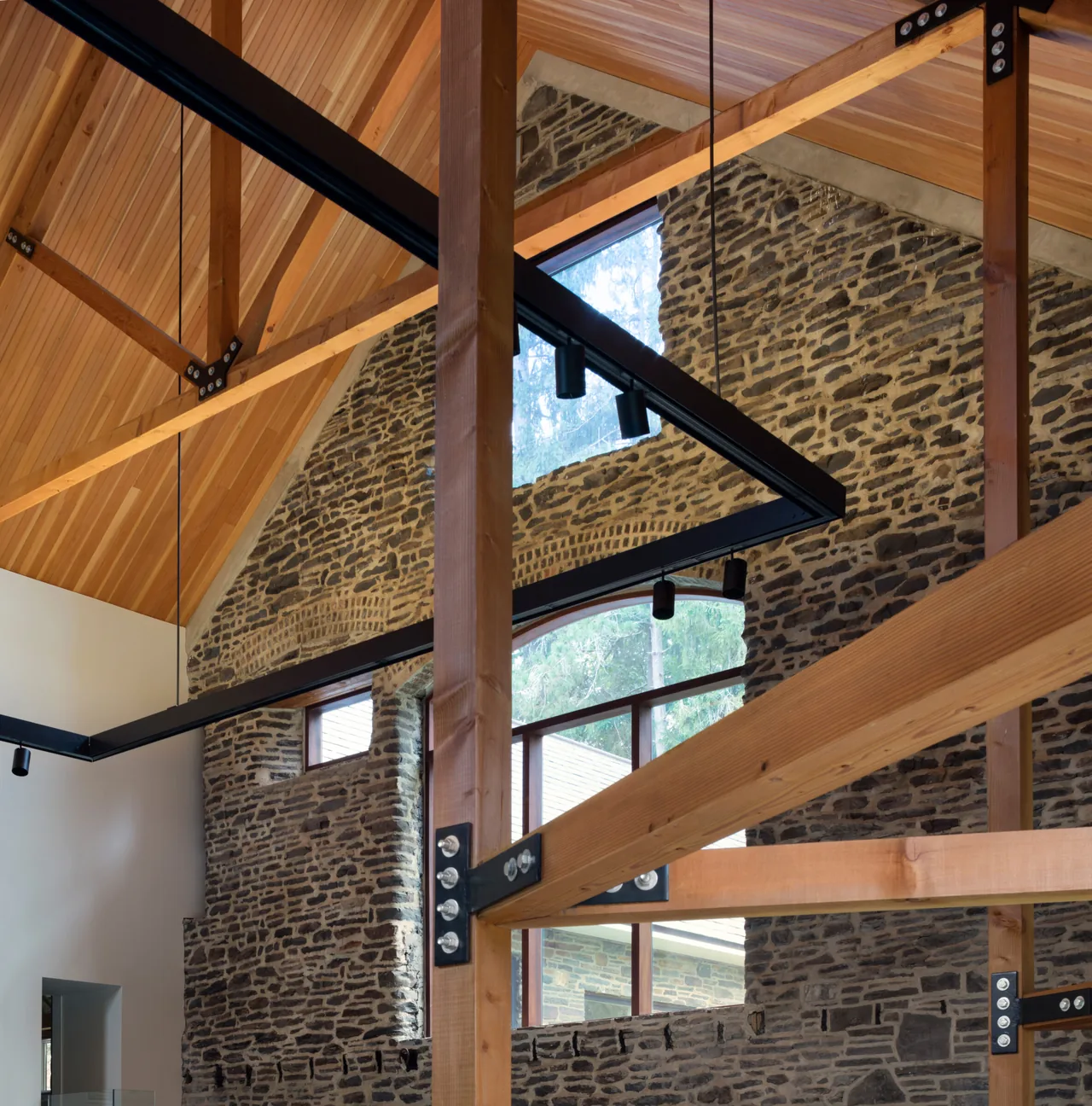 Exposed wooden trusses and arched glass window highlight the vaulted ceiling of this renovated barn interior.