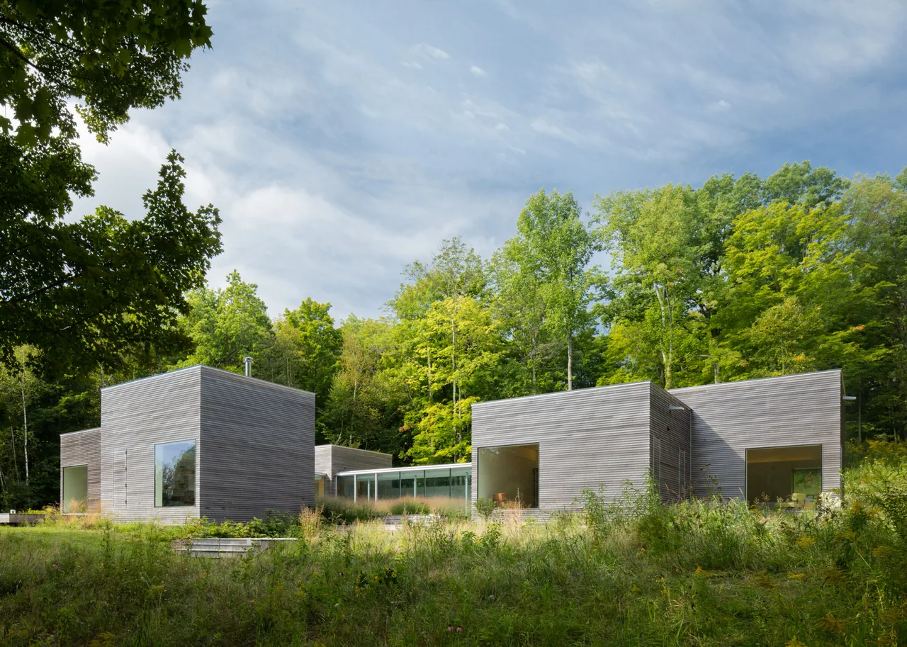 Modern rectangular wooden buildings surrounded by greenery under a partly cloudy sky.