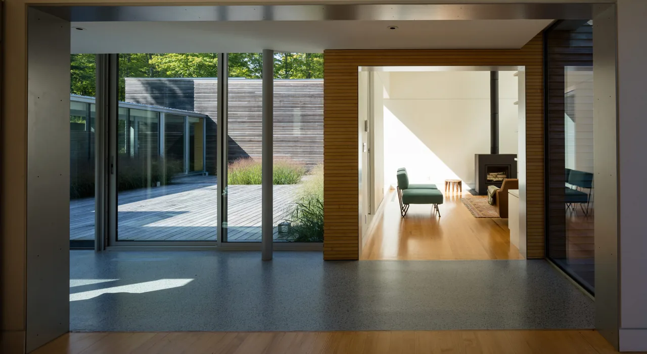 View from inside through glass doors of an artist retreat showing wood-paneled walls, sliding glass doors to a rear deck, and a living room with fireplace.