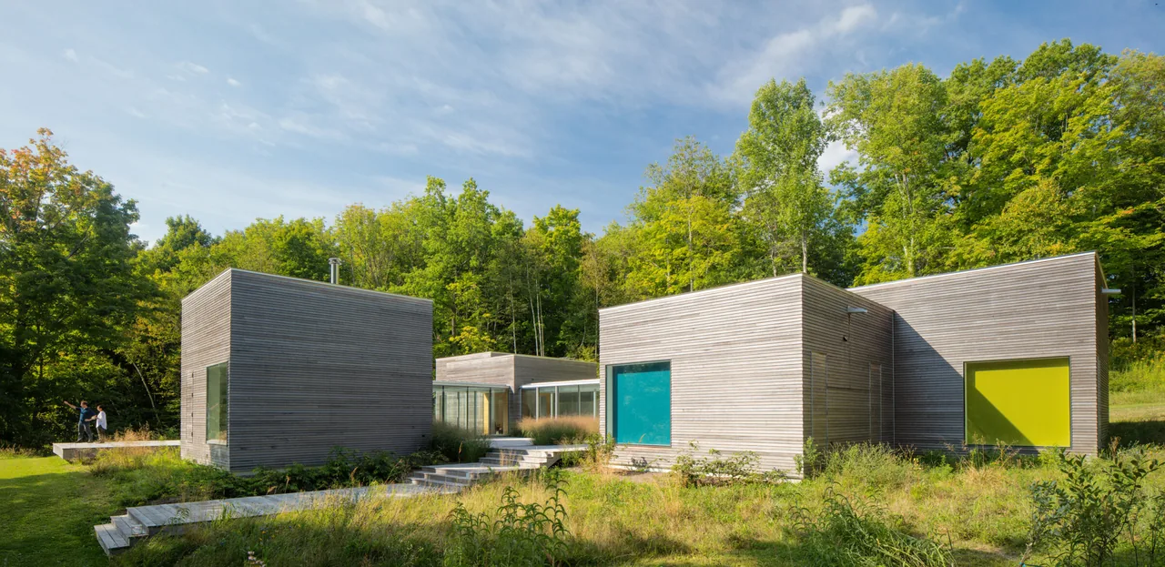 Artist Retreat features connected cubic volumes with horizontal wood siding set in a natural wooded landscape.