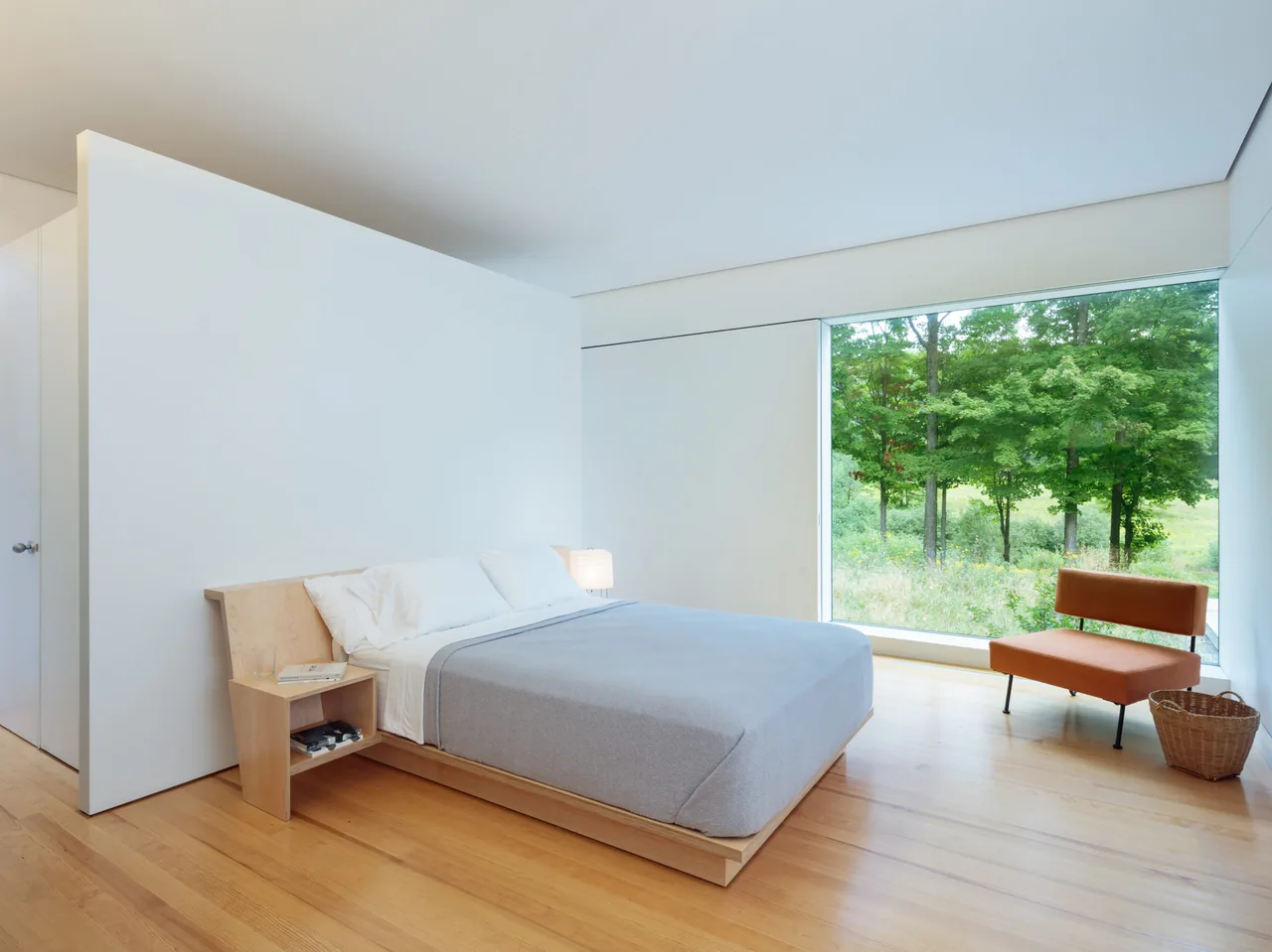 Bedroom features a low platform bed with built-in shelving and a large picture window facing a wooded landscape.