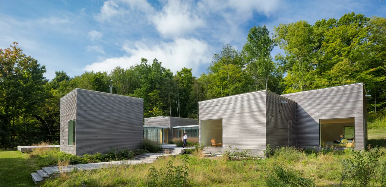 The Artist Retreat features connected cubic volumes with horizontal wood siding nestled in greenery.