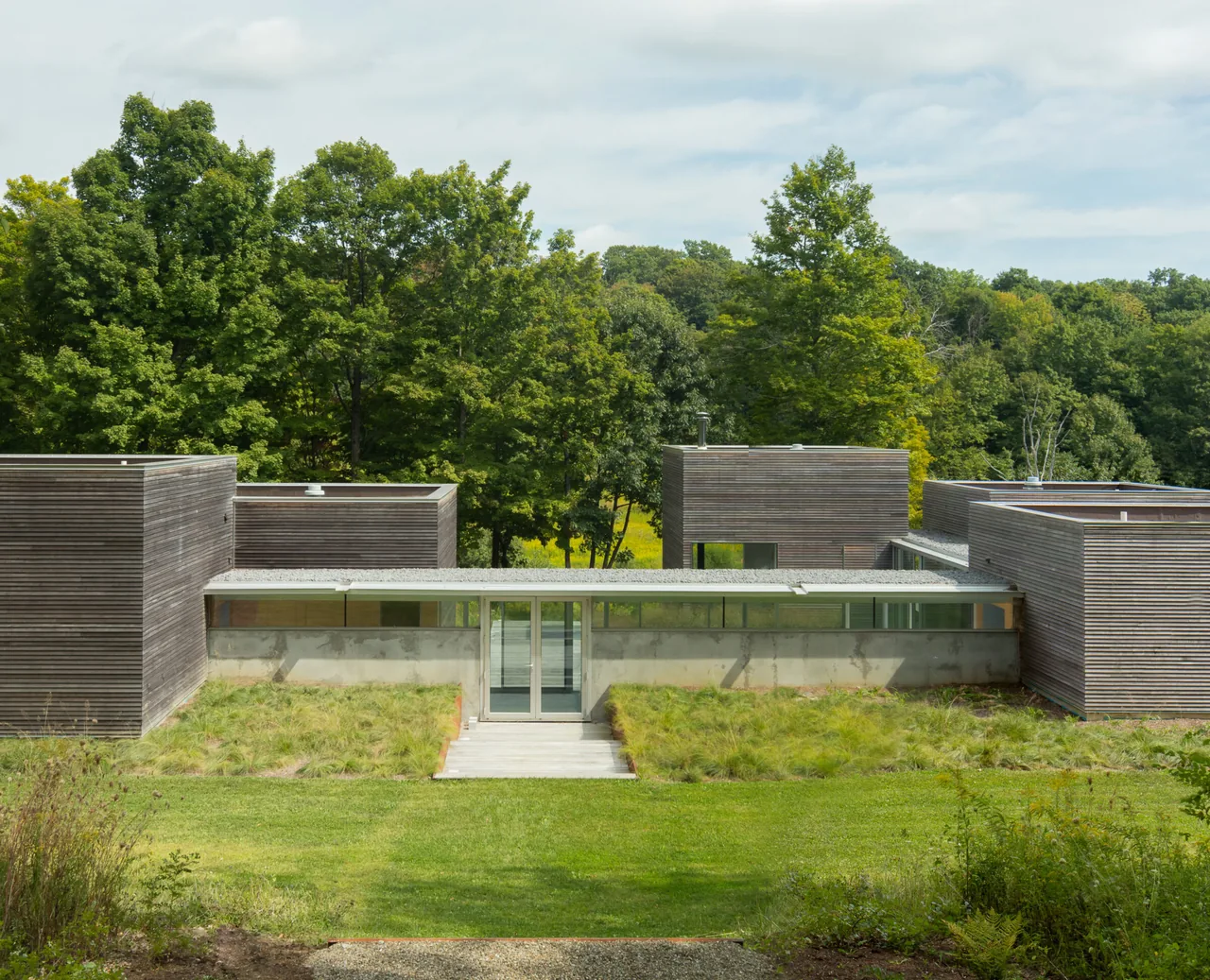The Artist Retreat features a modern design with wood siding and green roofing, situated in a forested area near New York.