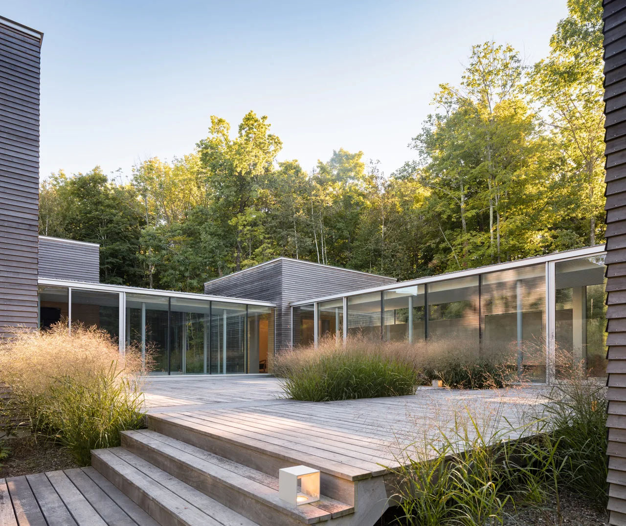 The Artist Retreat features connected boxy volumes with horizontal wood siding and a large deck surrounded by natural landscaping.