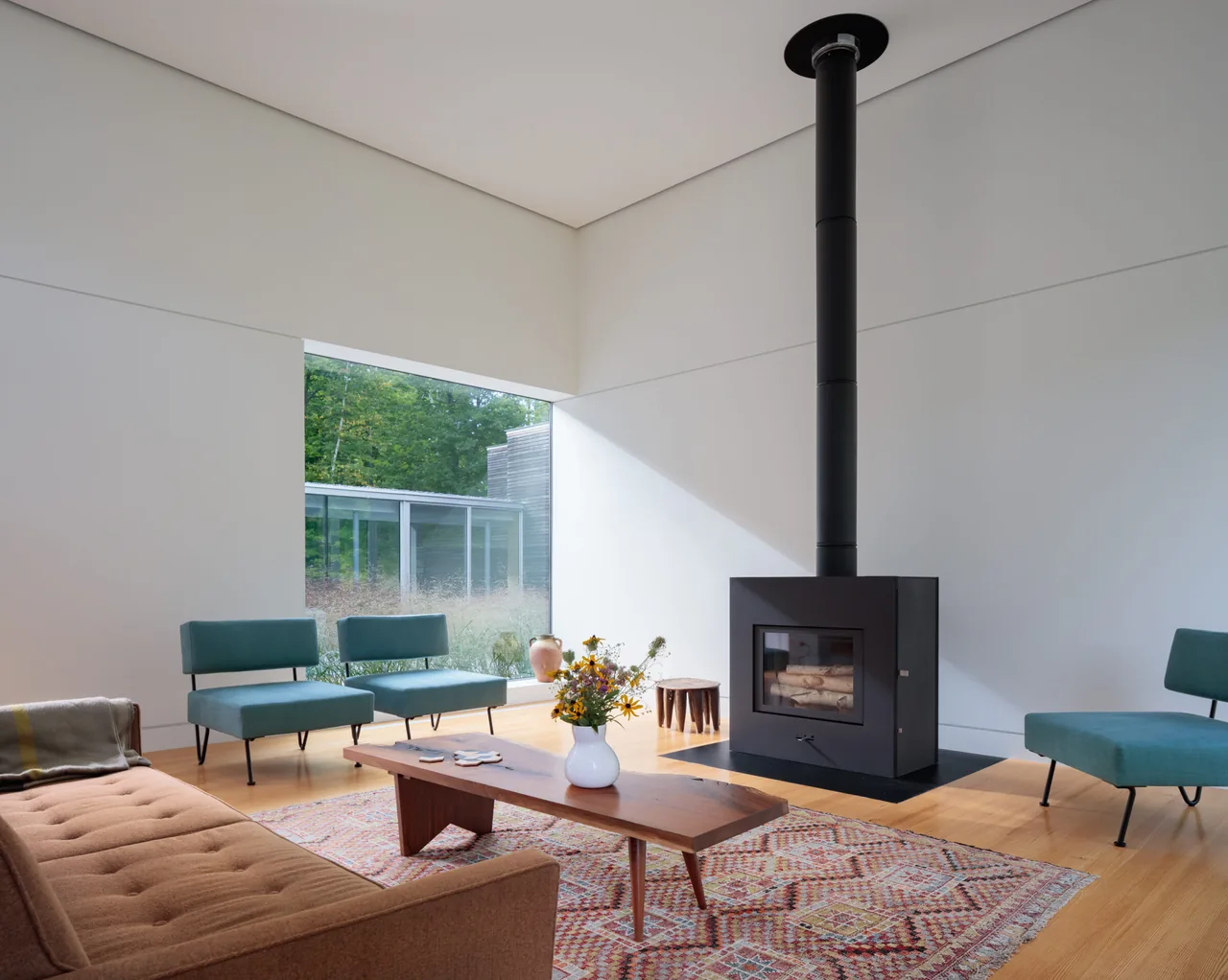 A serene living area features a black freestanding wood stove and minimalist furniture with views to a green courtyard.
