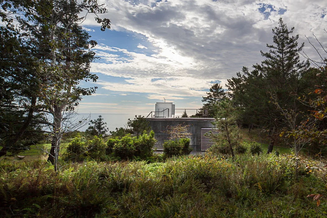 Concrete building nestled within lush vegetation and overlooking a coastal landscape at East House.