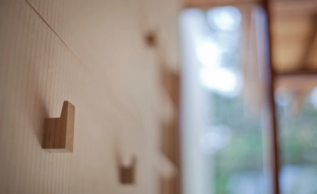 Light wood wall paneling with small wooden hooks and a blurred vertical window opening behind.